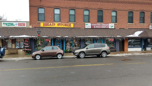 A row of small shops with colorful signs, holiday decorations, and parked cars on a snowy street.