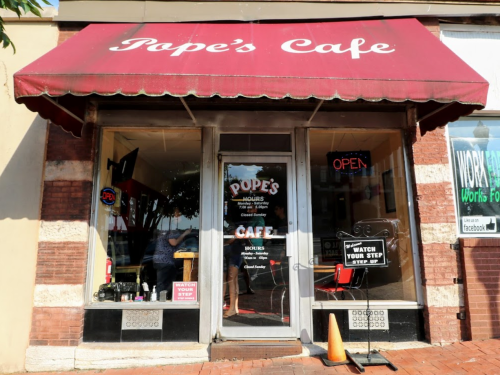 Exterior of Pope's Cafe with a red awning, open sign, and a "Watch Your Step" warning near the entrance.