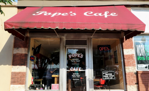 Exterior of Pope's Cafe with a red awning, open sign, and a notice to watch your step.