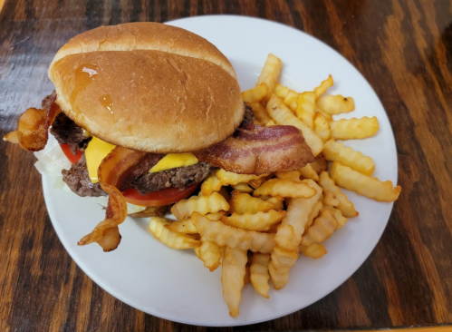 A cheeseburger with bacon, lettuce, and tomato on a bun, served with a side of crinkle-cut fries on a white plate.