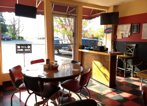 A cozy restaurant interior with a round table, chairs, and an open sign visible through the window.