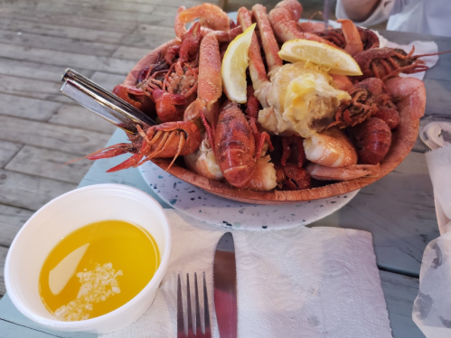 A bowl of assorted seafood, including shrimp and crawfish, garnished with lemon, alongside a cup of garlic butter.