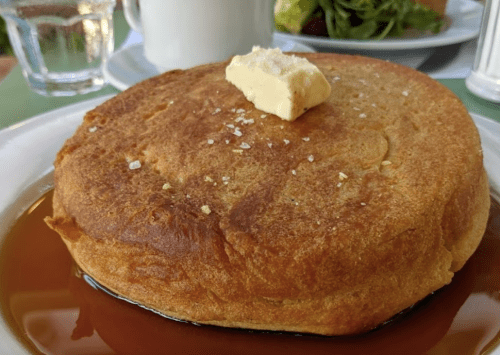 A thick, golden pancake topped with a pat of butter and drizzled with syrup, served on a white plate.