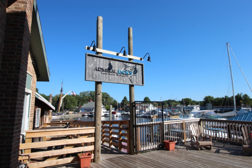 Sign for Admiral Jack's restaurant on a dock with boats and clear blue sky in the background.