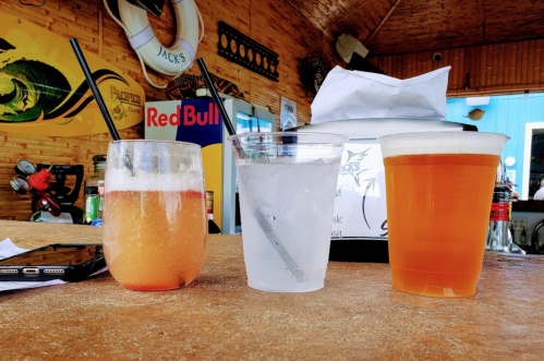 Three drinks on a bar counter: a cocktail, a clear drink with ice, and a pint of beer, with a phone nearby.