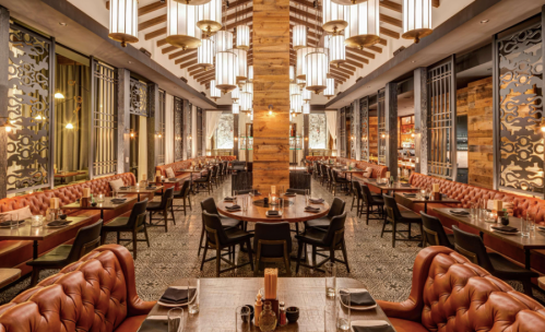 Elegant restaurant interior with wooden beams, plush seating, and ambient lighting, featuring round and rectangular tables.