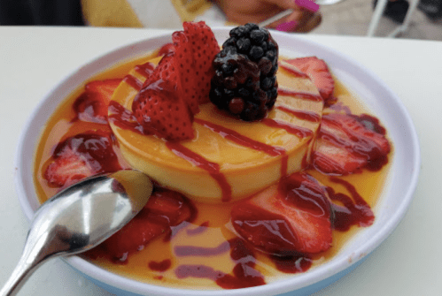 A creamy dessert topped with strawberries and blackberries, drizzled with berry sauce on a white plate.
