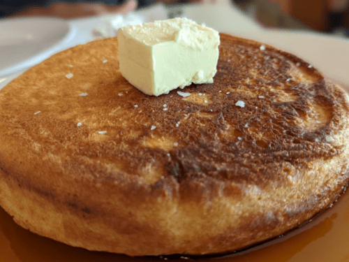 A golden-brown pancake topped with a pat of butter, resting on a plate.