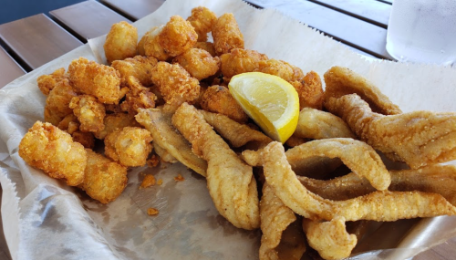 A plate of fried fish and hushpuppies, garnished with a lemon wedge, served on parchment paper.
