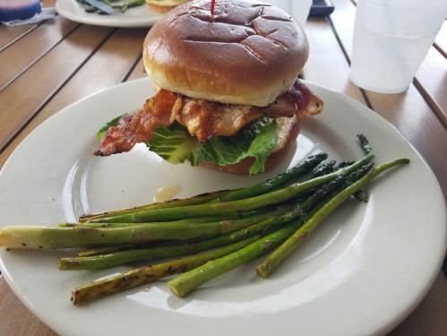 A sandwich with grilled chicken, bacon, and lettuce on a bun, served with grilled asparagus on the side.