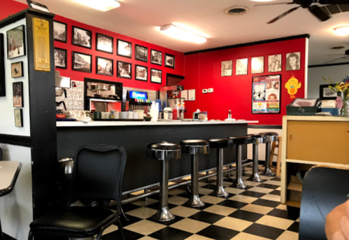 A retro diner interior with a red wall, black and white checkered floor, and chrome stools at the counter.