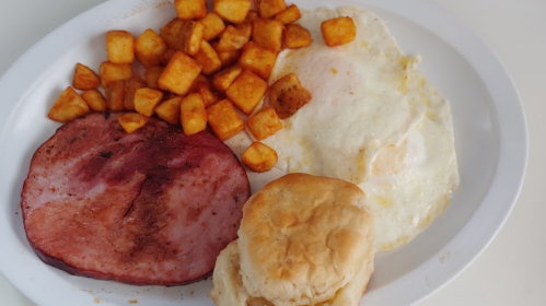A plate with fried eggs, ham, golden-brown potato cubes, and a biscuit.