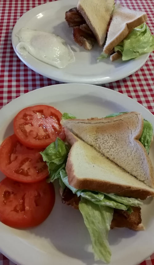 A plate with a sandwich filled with lettuce and fried chicken, accompanied by sliced tomatoes and a side of coleslaw.
