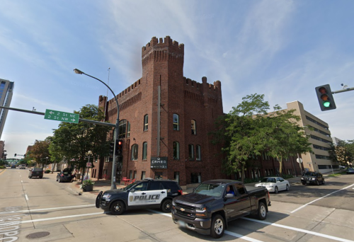 A brick building resembling a castle, with police cars parked at an intersection and traffic lights visible.