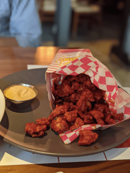 A plate with a paper cone filled with crispy fried chicken and a small bowl of dipping sauce on the side.