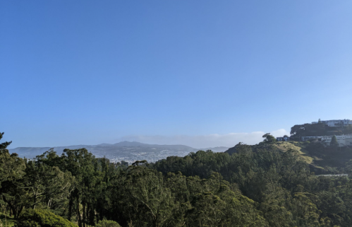 A scenic view of rolling hills and trees under a clear blue sky, with distant mountains in the background.