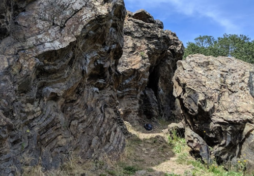 Rocky landscape featuring textured stone formations and a small pathway leading into a shaded area.