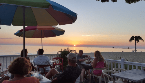 A beachside restaurant scene at sunset, with colorful umbrellas and diners enjoying the view of the ocean.