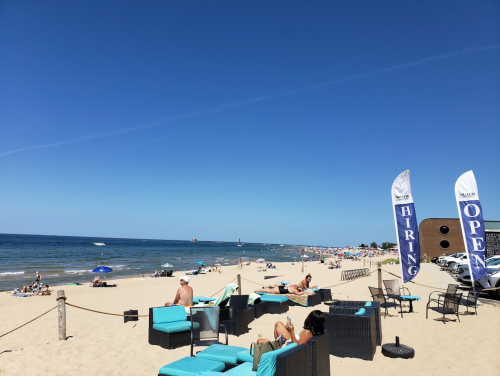 A sunny beach scene with people relaxing, beach chairs, and flags indicating "Hiring" and "Open" in the background.