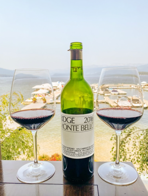 A bottle of Ridge Monte Bello 2016 wine with two glasses, overlooking a marina and scenic water view.