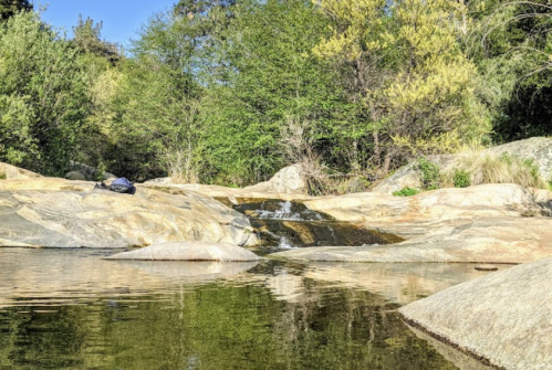 A serene rocky landscape with a small waterfall and lush greenery reflected in calm water.