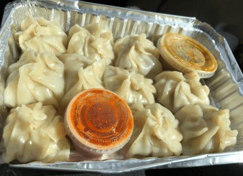 A tray of dumplings with two containers of dipping sauce, one red and one yellow, on a dark background.