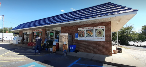 A small restaurant with a blue roof, featuring signs for Indian and Nepali food, and a customer at the entrance.