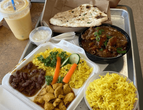 A tray with two types of yellow rice, chicken, beans, salad, a naan, and a drink.