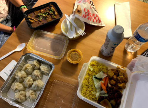 A table with various food containers, including dumplings, curry, rice, and drinks, alongside utensils and napkins.