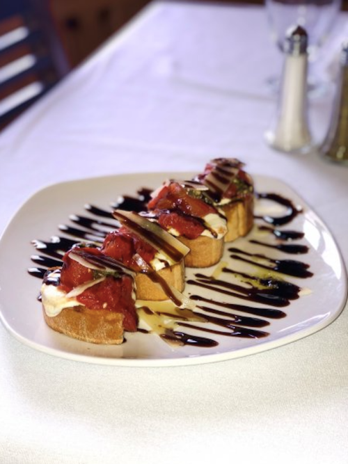 A plate of bruschetta topped with tomatoes and drizzled with balsamic glaze, served on a white tablecloth.