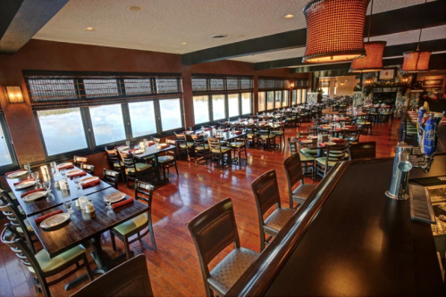 A spacious restaurant interior with wooden tables, chairs, and large windows offering a scenic view.