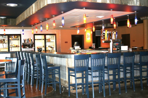 A modern bar area with high stools, colorful pendant lights, and a sleek counter in a cozy setting.