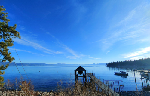 A serene lake view with a dock, boats, and trees under a clear blue sky.