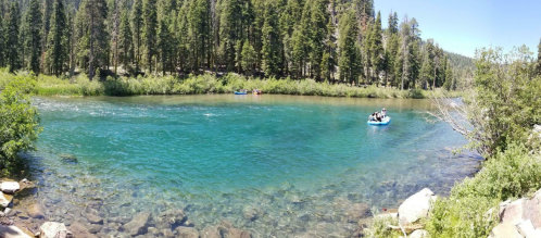 A serene river scene with clear blue water, surrounded by lush green trees and people in a boat.
