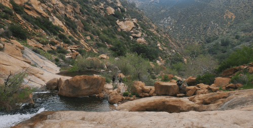A scenic view of rocky terrain with a small stream and lush greenery in a mountainous landscape.