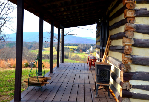 A rustic porch with wooden logs, a swing, and a view of rolling hills and mountains in the background.