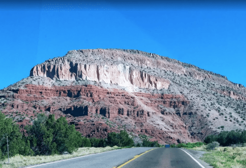 A scenic view of a red rock mountain under a clear blue sky, with a road leading towards it.