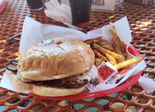 A burger with melted cheese and bacon, served with fries and ketchup on a red tray.