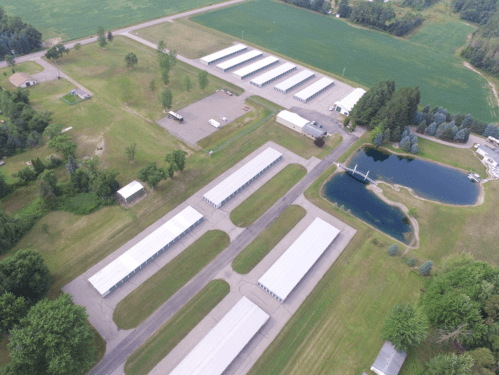 Aerial view of a storage facility with several buildings, a pond, and green fields surrounding the area.
