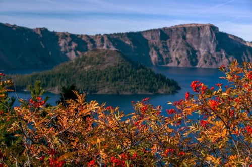 A scenic view of Crater Lake with vibrant autumn foliage in the foreground and rugged cliffs in the background.