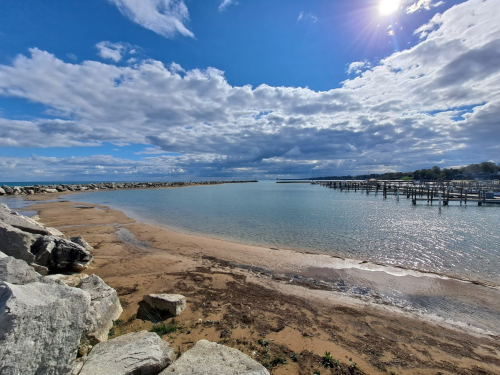 A serene beach scene with rocky shorelines, calm water, and a cloudy sky reflecting sunlight.