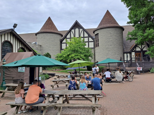 A group of people dining at outdoor tables in front of a castle-like building with green umbrellas.