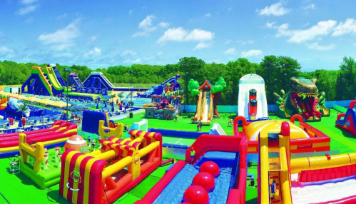 A vibrant outdoor amusement park featuring various inflatable slides, bounce houses, and play areas under a clear blue sky.