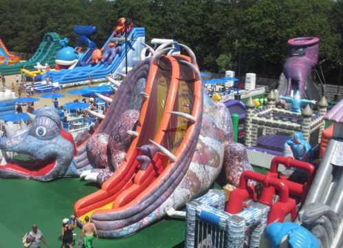 A colorful inflatable water park featuring a dragon slide and various other attractions in a sunny outdoor setting.