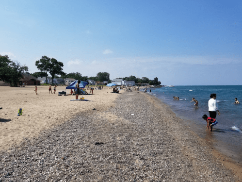 A sandy beach with people enjoying the sun, swimming, and playing near the water on a clear day.