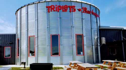Exterior of Triplets Barbecue, featuring a round metal building with red signage and picnic tables outside.