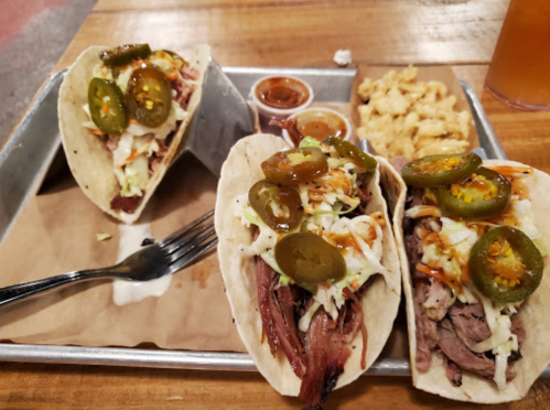 Three tacos filled with pulled meat, topped with jalapeños and slaw, served with a side of macaroni and cheese.