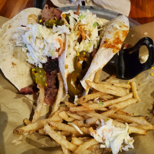 Two tacos filled with meat and toppings, served with a side of fries on a paper-lined plate.