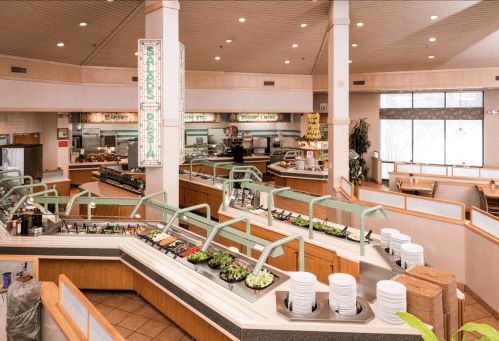 A spacious restaurant interior featuring a salad and pasta bar with various toppings and seating areas.