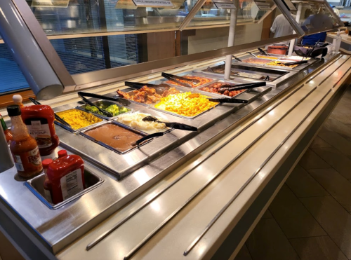 A buffet line featuring various dishes, including macaroni and cheese, vegetables, and sauces in containers.